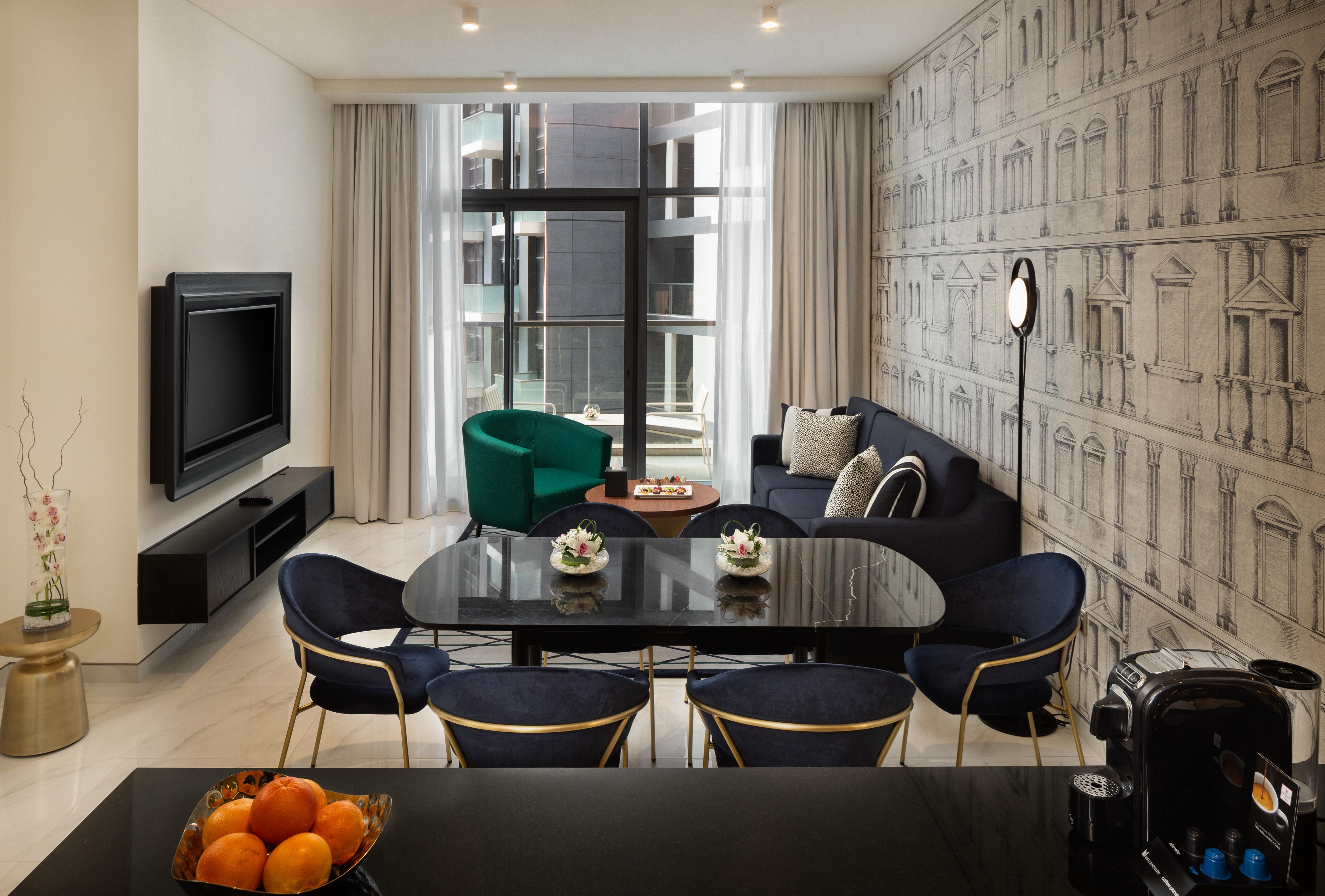 Апарт готель Millennium Atria Business Bay Дубай Екстер'єр фото The photo shows a modern living space that includes a cozy seating area and dining setup. On the left, there is a large television mounted on the wall. The living room features a blue sofa and a green accent chair, creating a stylish contrast. A smal