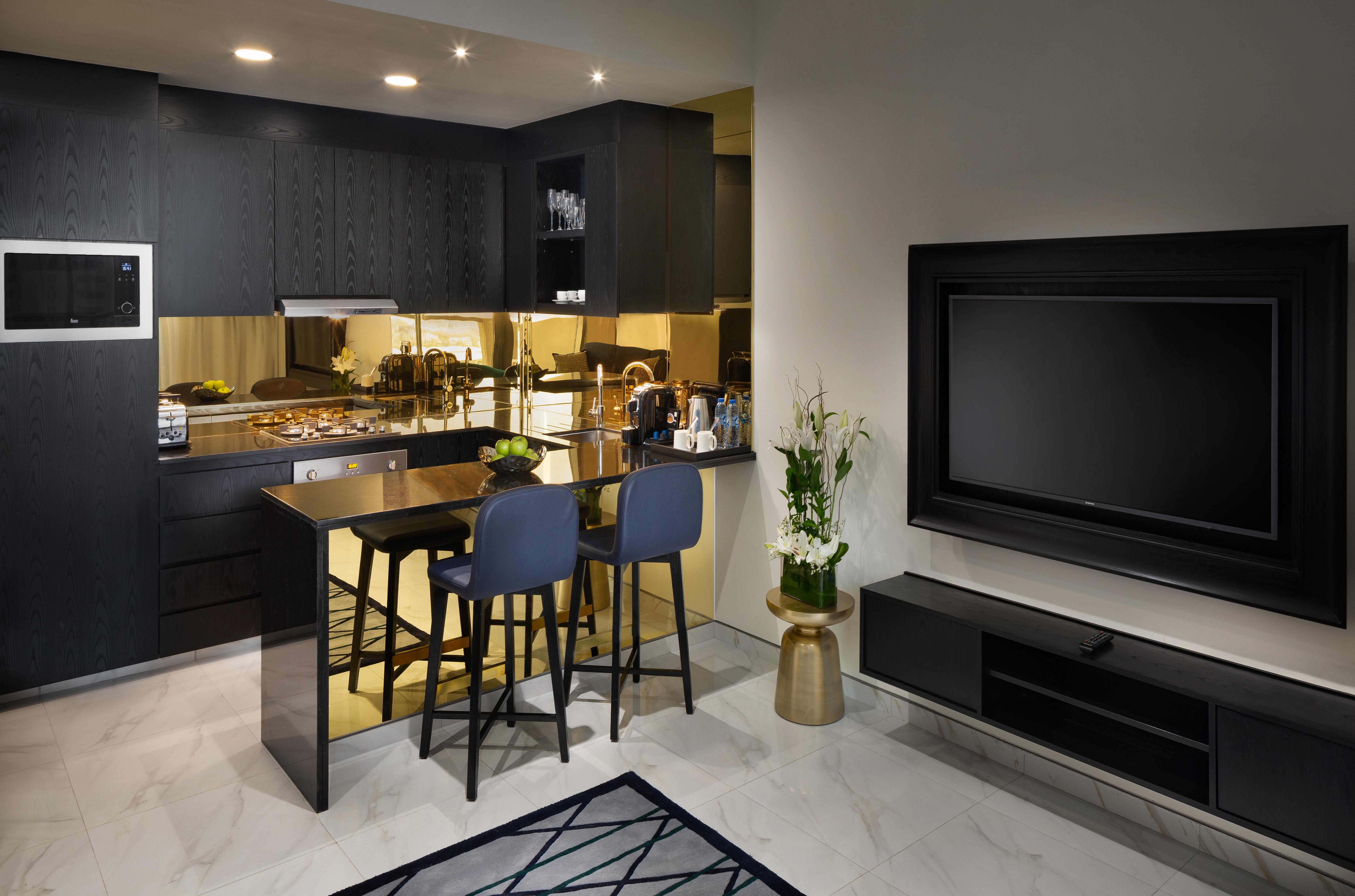 Апарт готель Millennium Atria Business Bay Дубай Екстер'єр фото The photo depicts a modern kitchen and living area. The kitchen features dark cabinetry with a clean design, showcasing various appliances, including a stovetop and possibly an oven. There is a kitchen island with two stools, suggesting a space for c