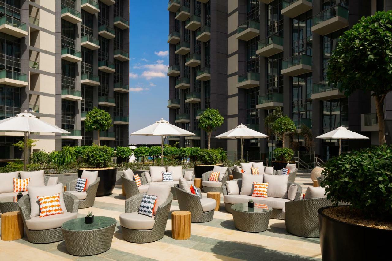 Апарт готель Millennium Atria Business Bay Дубай Екстер'єр фото The photo shows a modern outdoor lounge area, featuring several comfortable seating arrangements made of soft, stylish lounge chairs and round tables. The seating is adorned with colorful pillows, adding a pop of color to the neutral tones of the fur